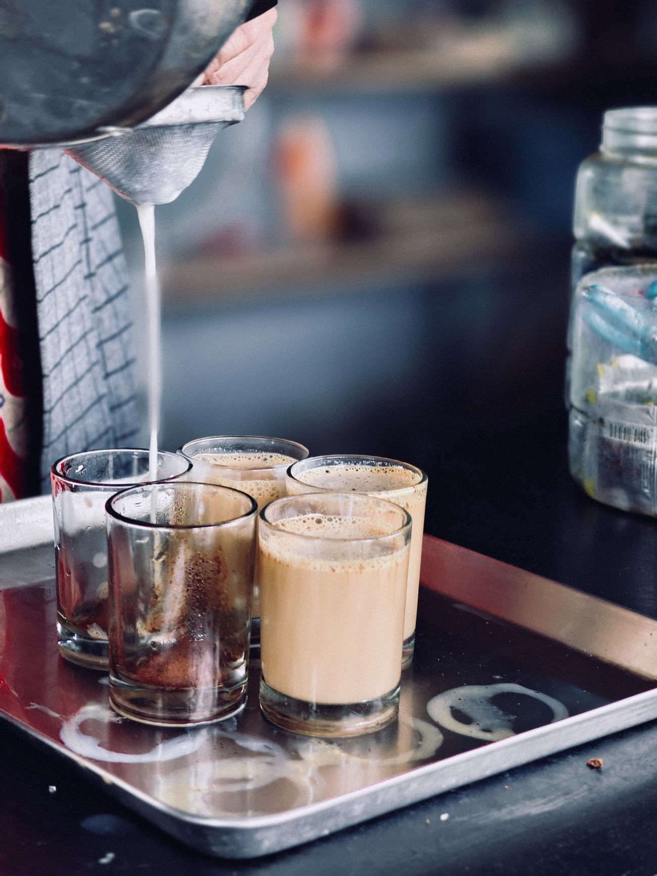 A vendor pouring chai into small glasses